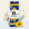 Front-facing photo of the Barkin’ Bandanas beeswax wrap set, showing all four sizes folded in retail packaging. The blue dog pattern with yellow bandanas and coordinating yellow gingham is visible, styled with illustrated flowers.